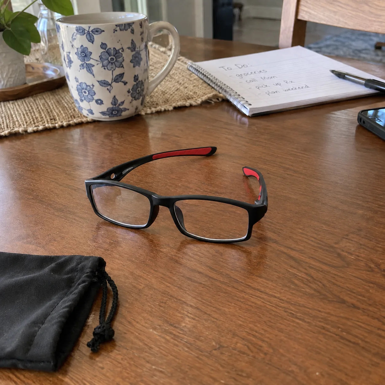 Black and red glasses on a dining table beside a notebook and pouch