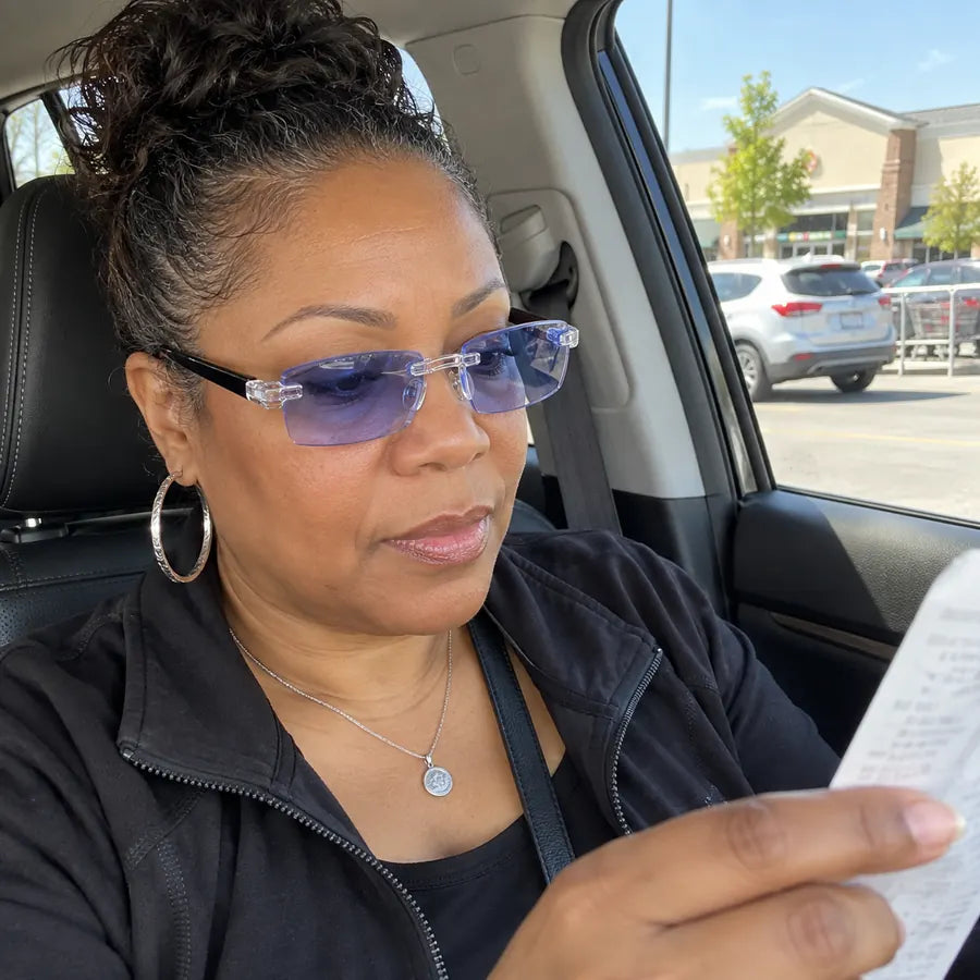 Woman wearing blue-light rimless glasses while reading a receipt in a car